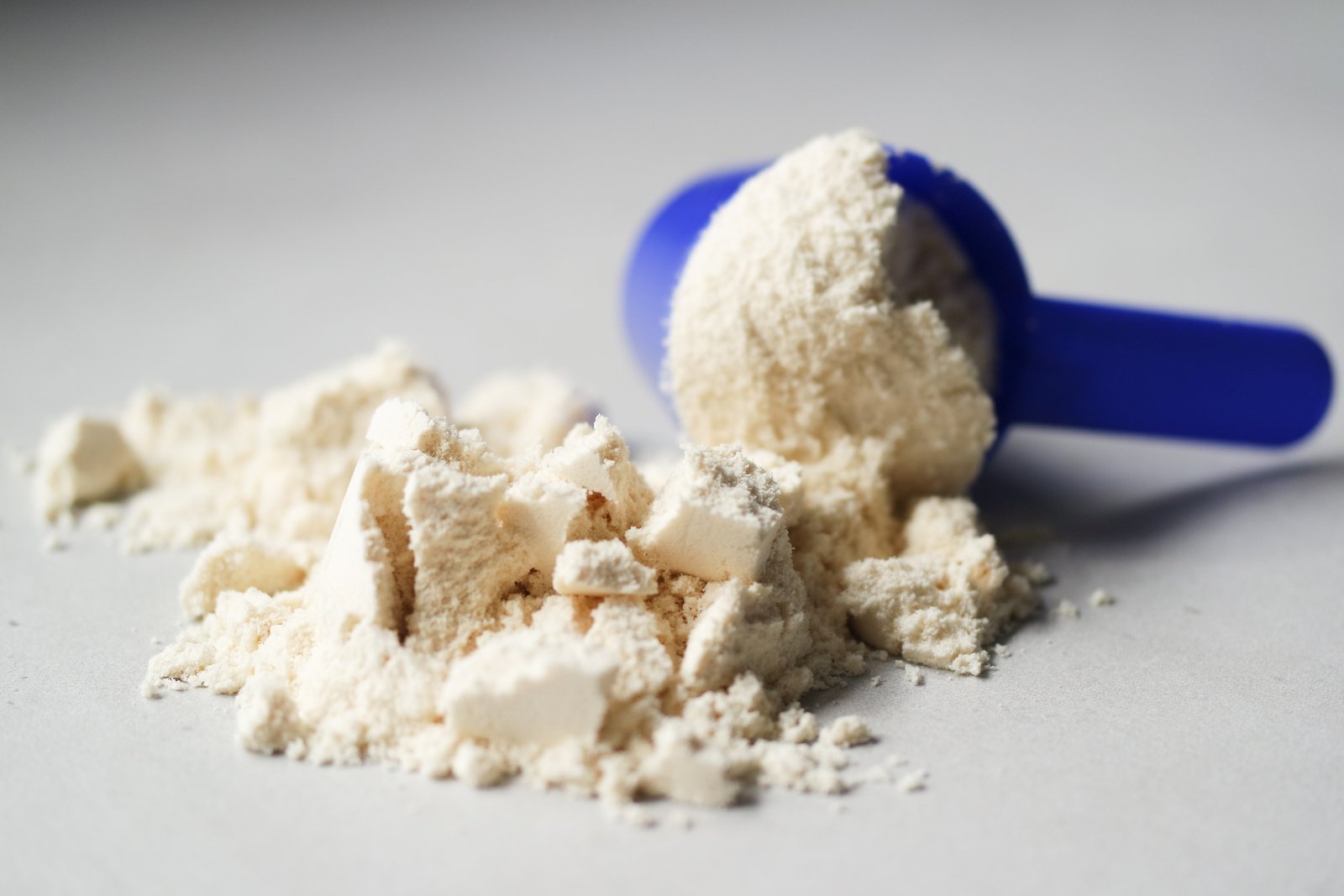 Muỗng đong đầy bột whey protein, chụp cận cảnh bên cạnh đĩa tạ