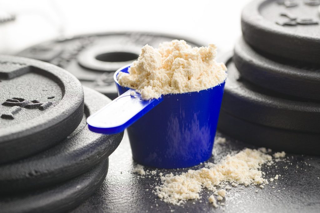 Muỗng đong đầy bột whey protein đặt trên bánh tạ — mỗi muỗng bột mang theo một lượng calo cụ thể phải cộng vào tổng ngày