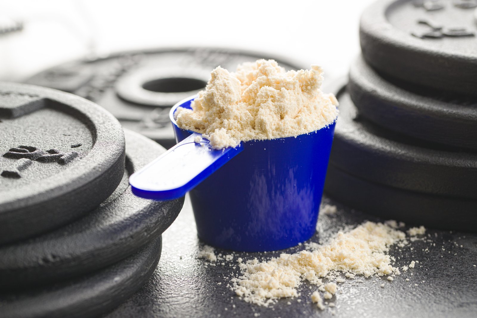 Muỗng đong đầy bột whey protein đặt trên bánh tạ — mỗi muỗng bột mang theo một lượng calo cụ thể phải cộng vào tổng ngày