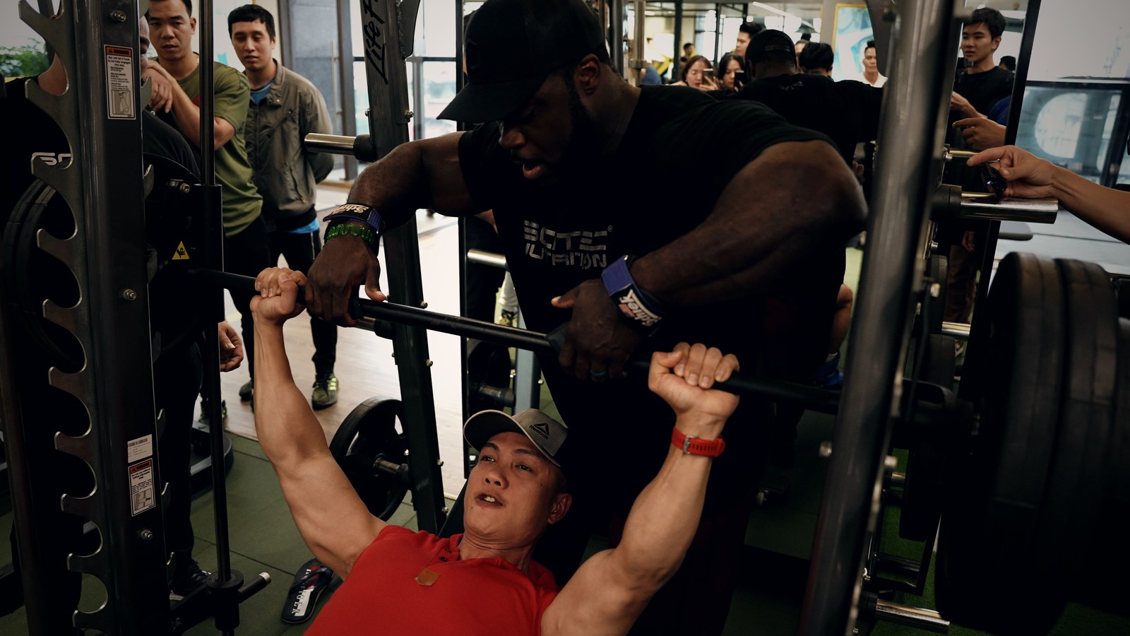 Brandon Curry đỡ thanh tạ khi Nguyễn Bảo Bằng đẩy ngực trên máy Smith