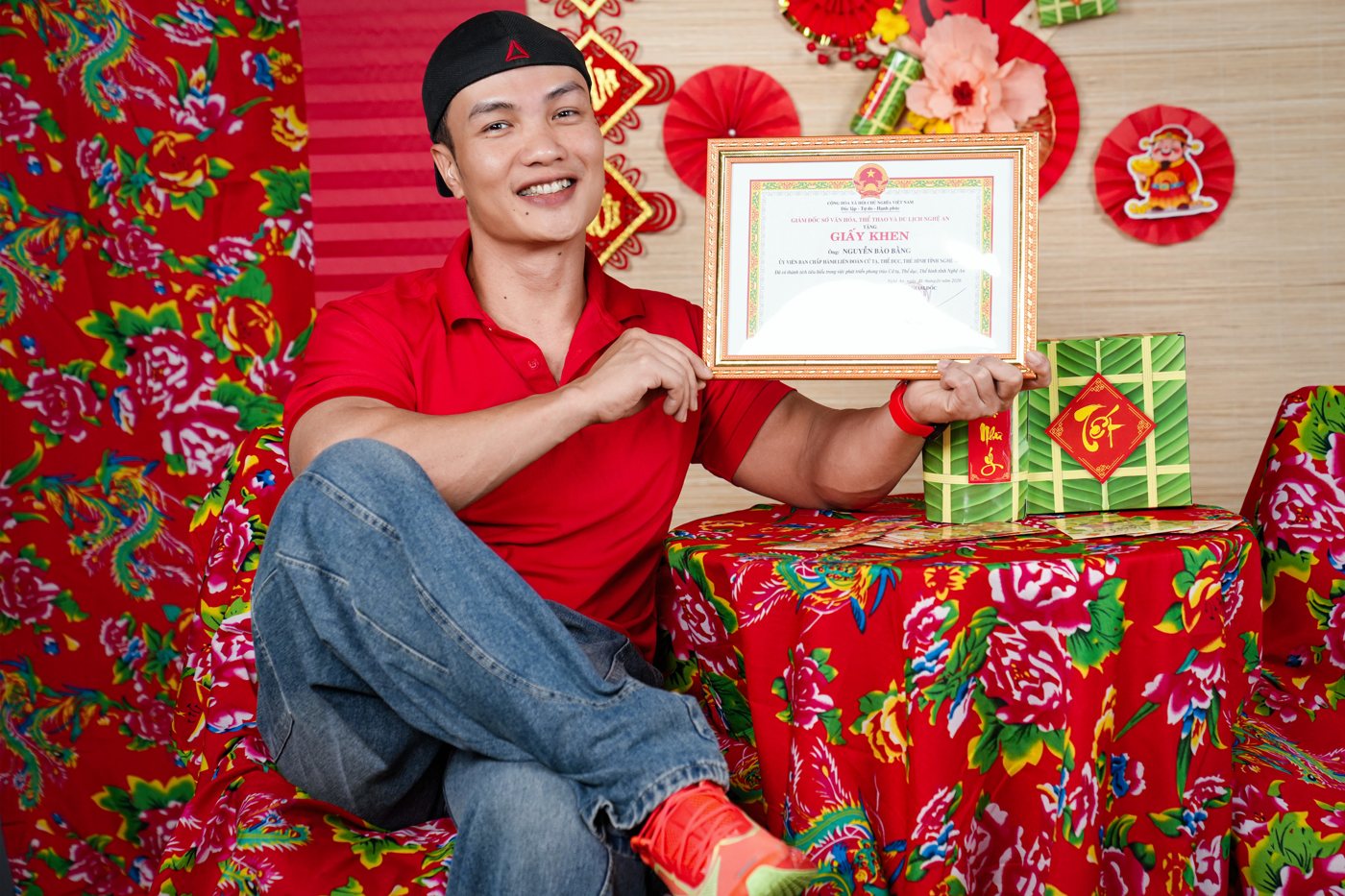 Nguyễn Bảo Bằng cầm giấy khen của Sở Văn hoá, Thể thao và Du lịch Nghệ An, chụp trên phông trang trí Tết tại phòng tập
