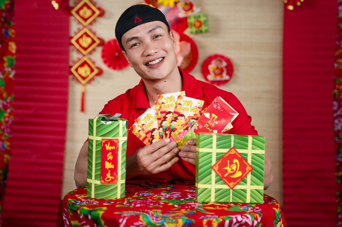 Nguyễn Bảo Bằng cầm bánh chưng và phong bao lì xì trên phông trang trí Tết tại phòng tập