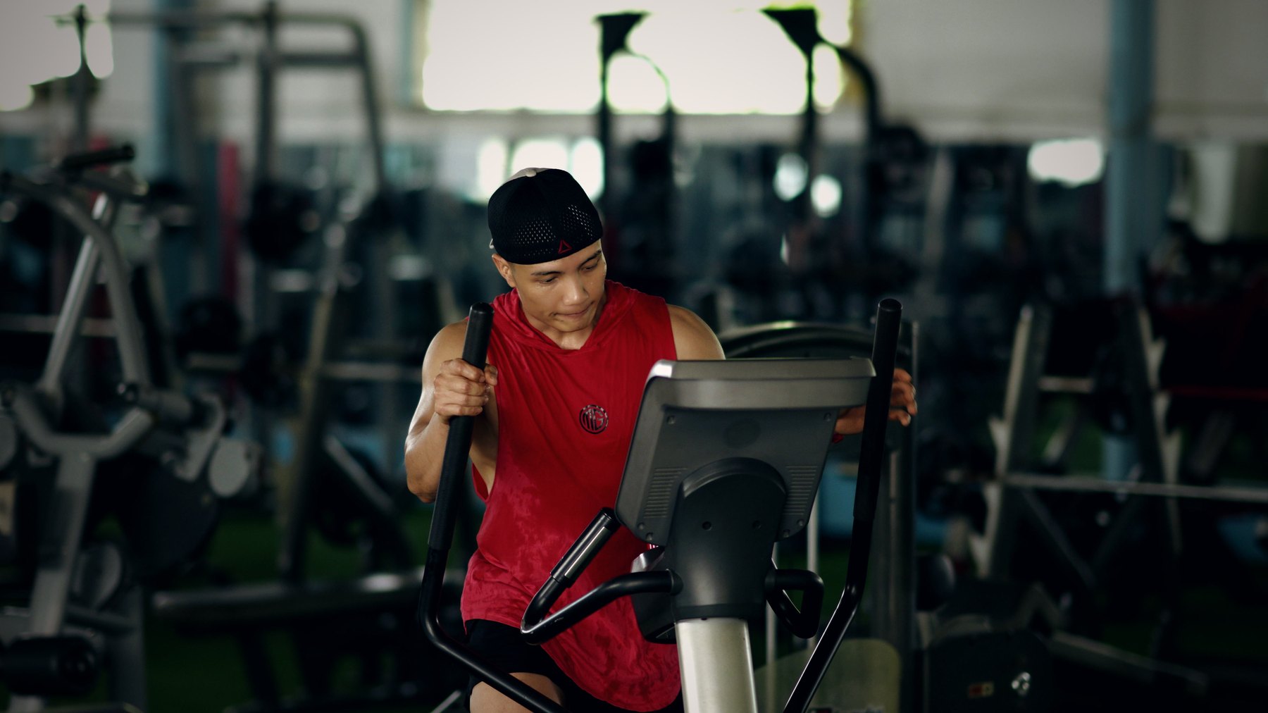 Nguyễn Bảo Bằng cúi người tập trên máy elliptical trong phòng gym