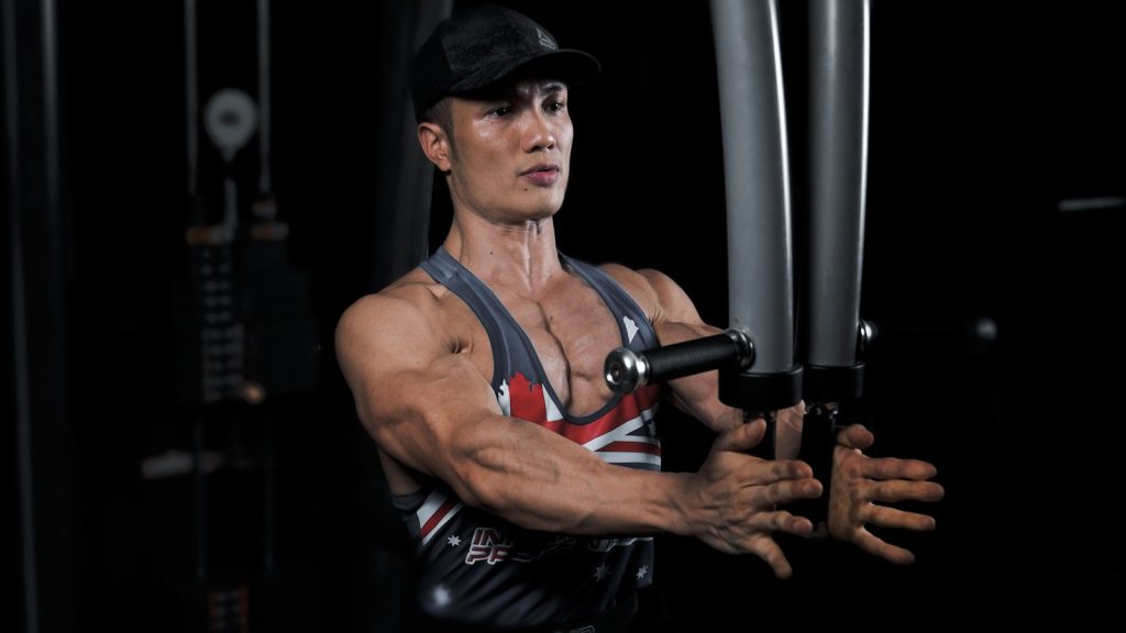 Huấn luyện viên Nguyễn Bảo Bằng tập ngực bằng máy cáp trong phòng gym, hai tay khép vào giữa ở cuối biên độ động tác fly