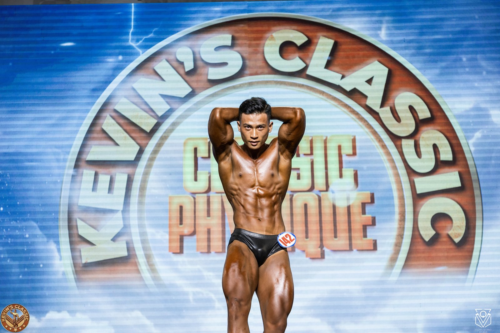 Vận động viên Classic Physique tạo dáng tay sau đầu, cơ bụng và đùi rõ