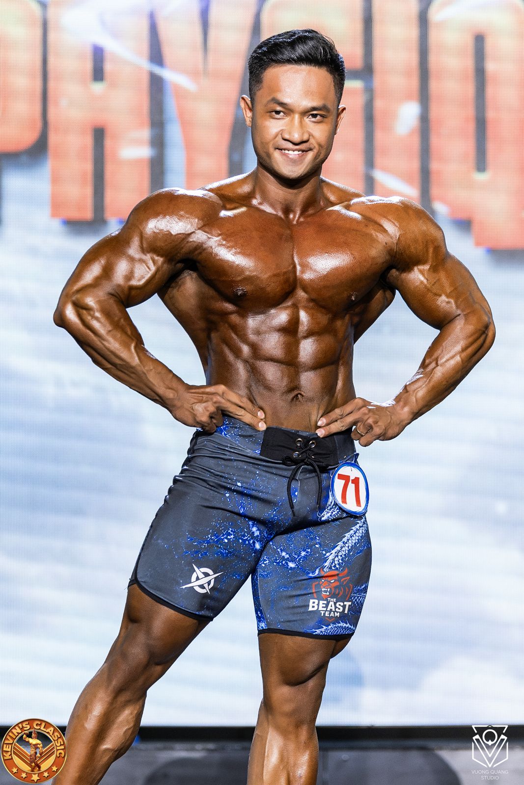 Vận động viên Men Physique cận cảnh, tay chống hông, cơ bụng nét