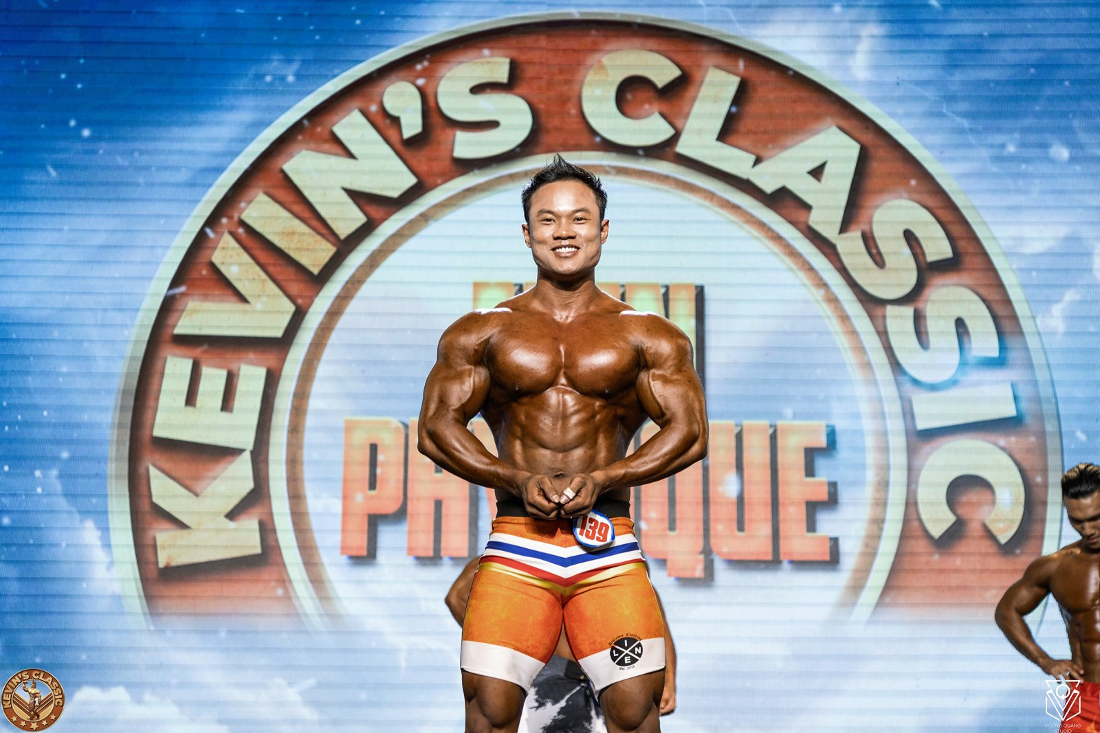 Vận động viên Men Physique mặc quần short dài, tư thế trước