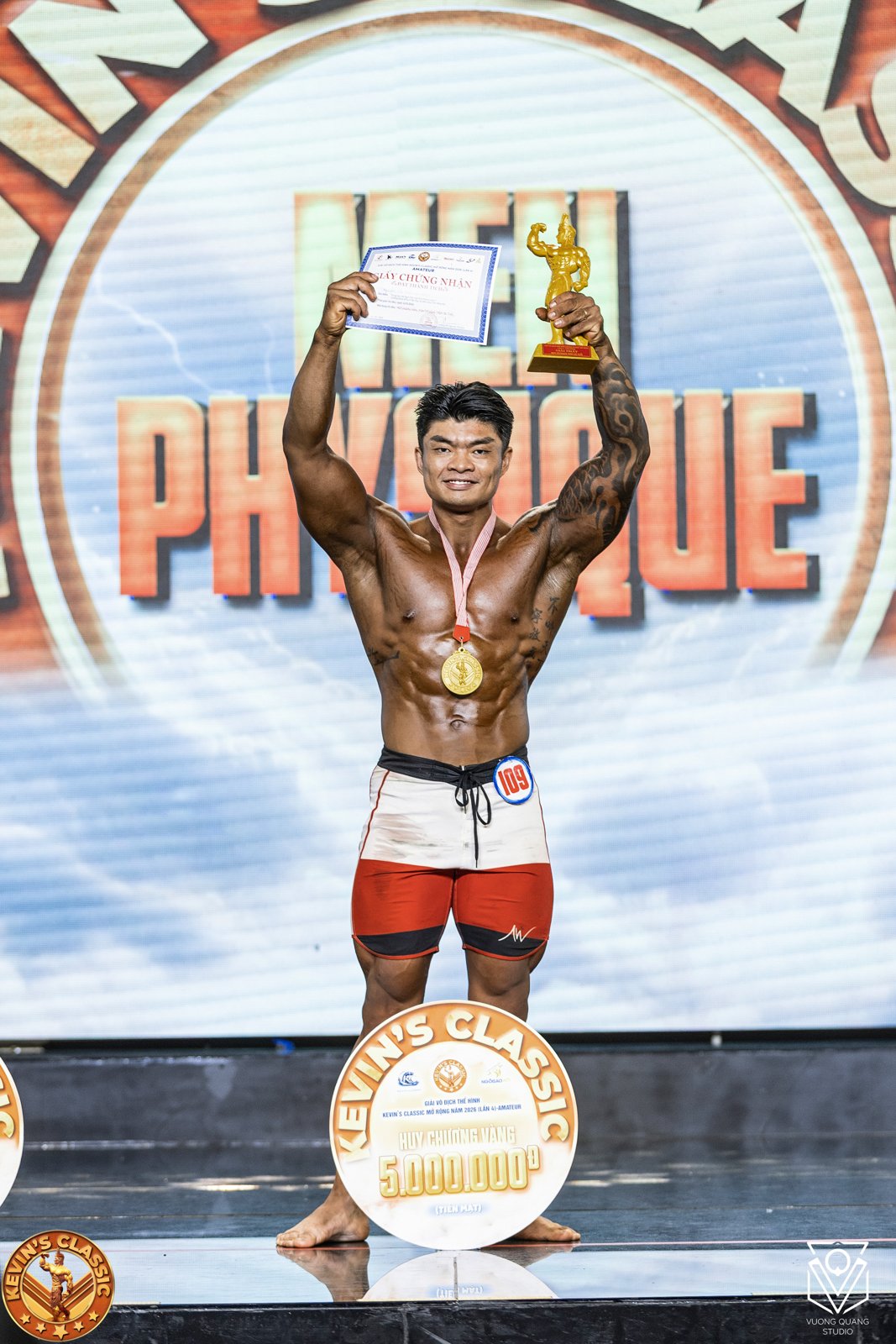 Vận động viên Men Physique giơ cúp và giấy chứng nhận, đeo huy chương vàng