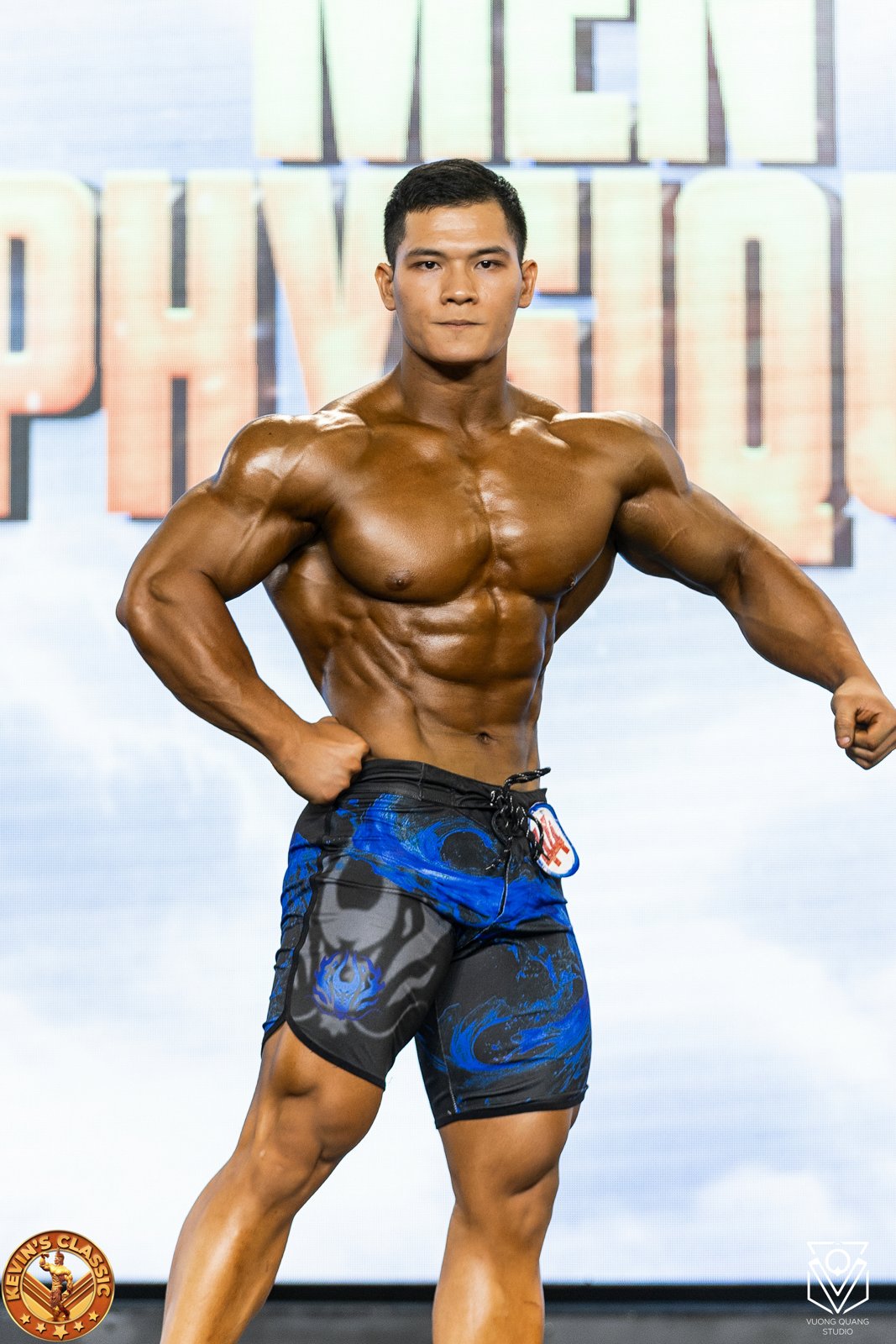 Vận động viên Men Physique mặc quần short dài làm tư thế trước trên sân khấu