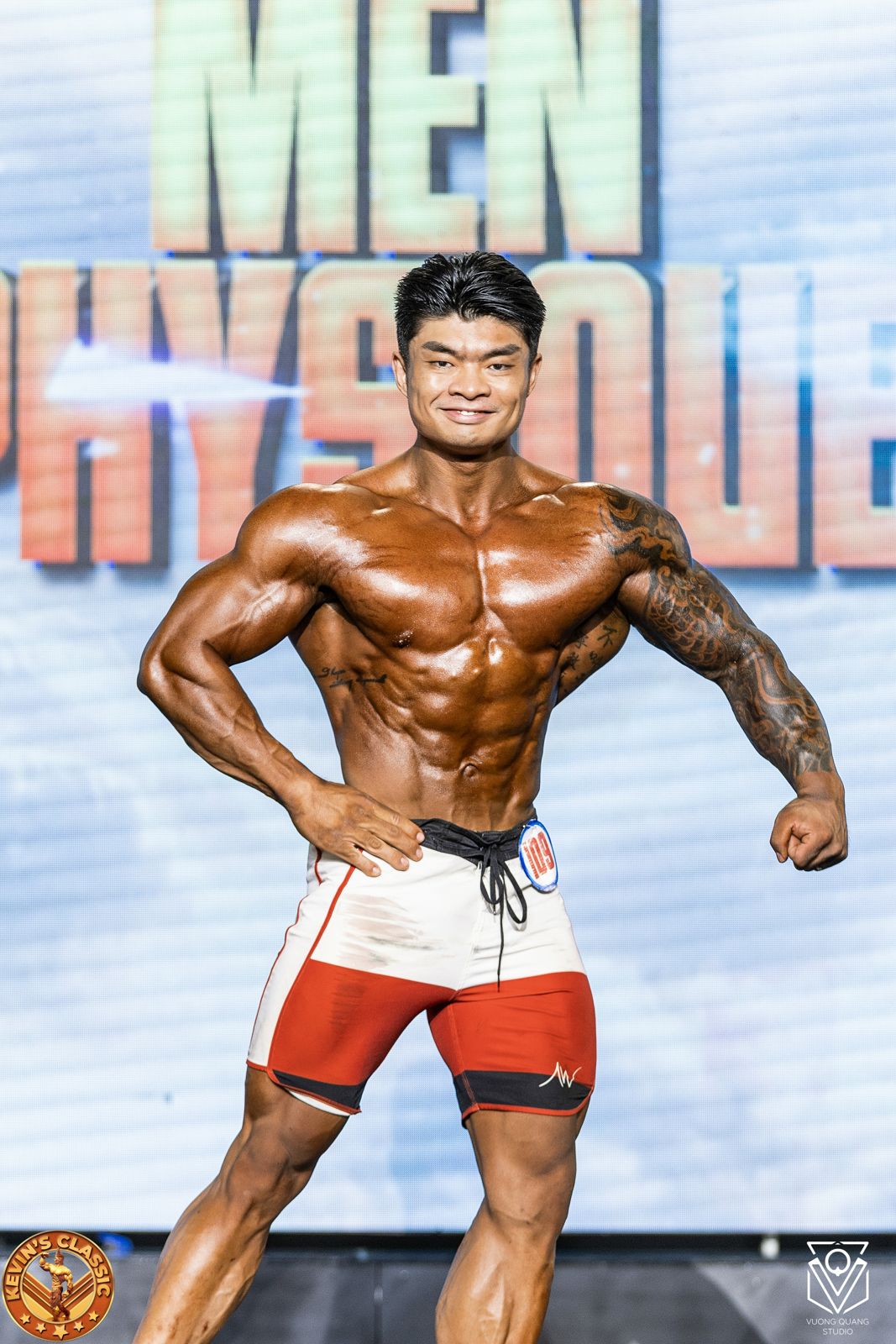 Vận động viên Men Physique vai rộng, eo nhỏ tạo dáng trước phông Men Physique