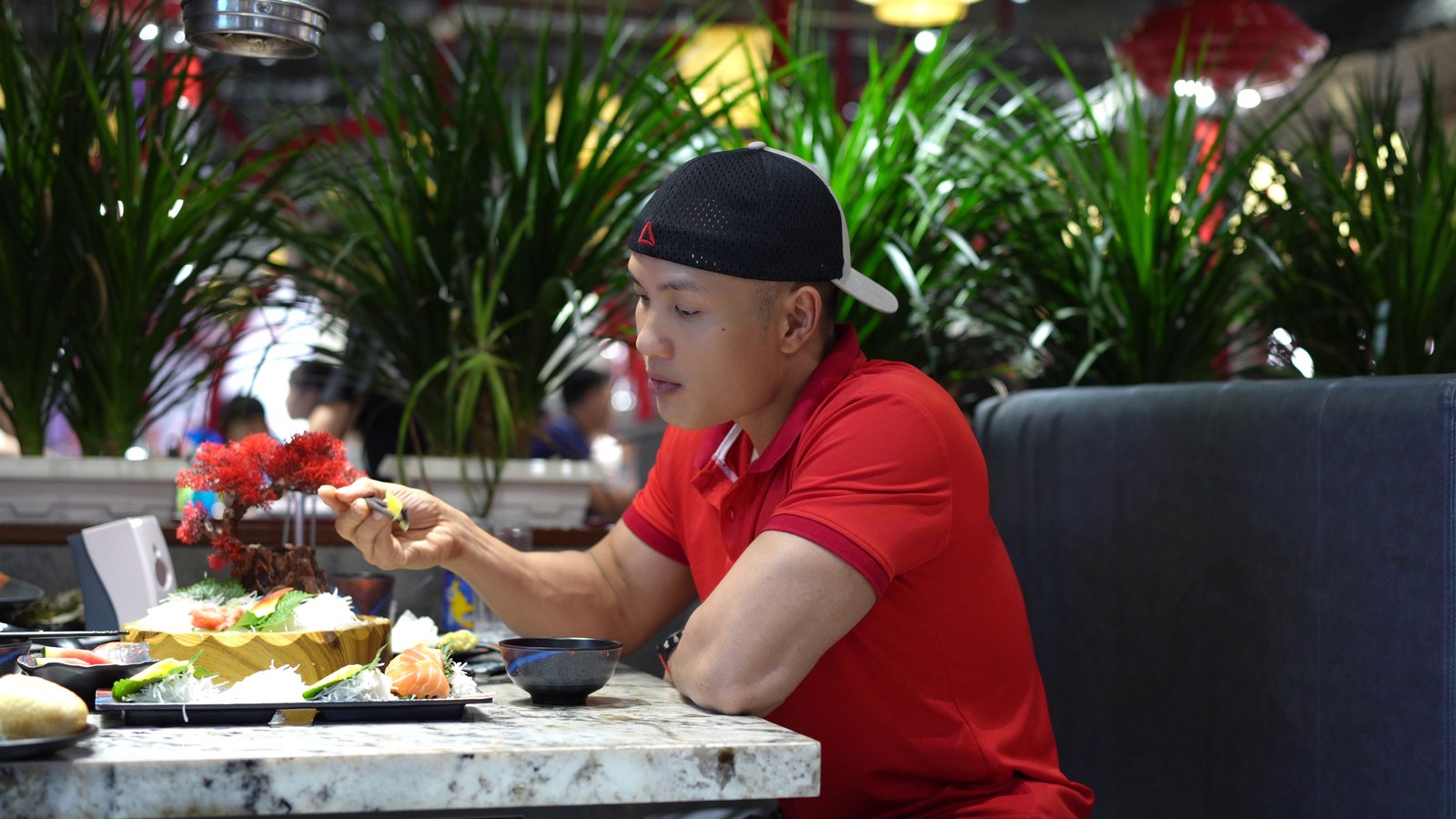 Nguyễn Bảo Bằng ngồi tại bàn ăn, đang chọn và gắp món từ đĩa thức ăn