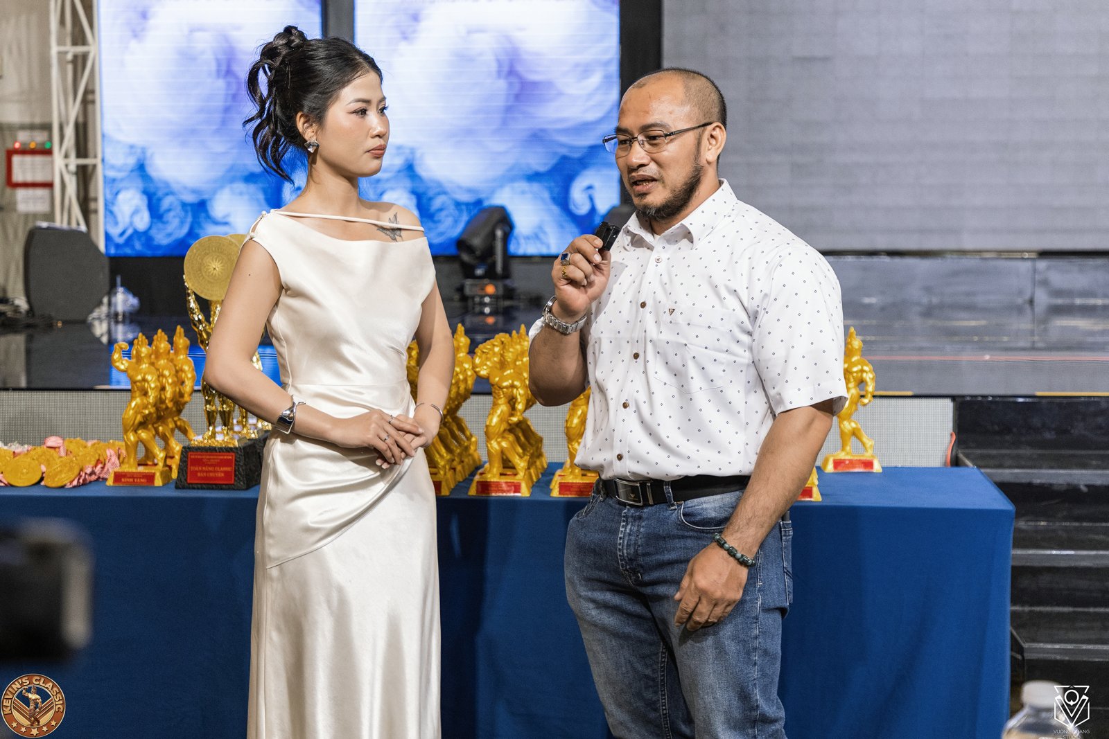 Nguyễn Thế Quý cầm micro trò chuyện cùng MC bên dãy cúp giải Kevin's Classic