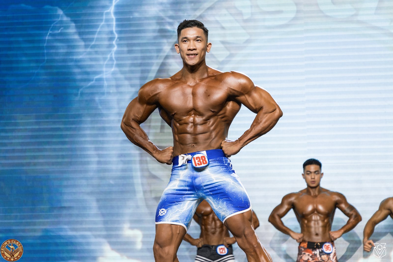 Vận động viên Men Physique tay chống hông, vai rộng, cơ căng