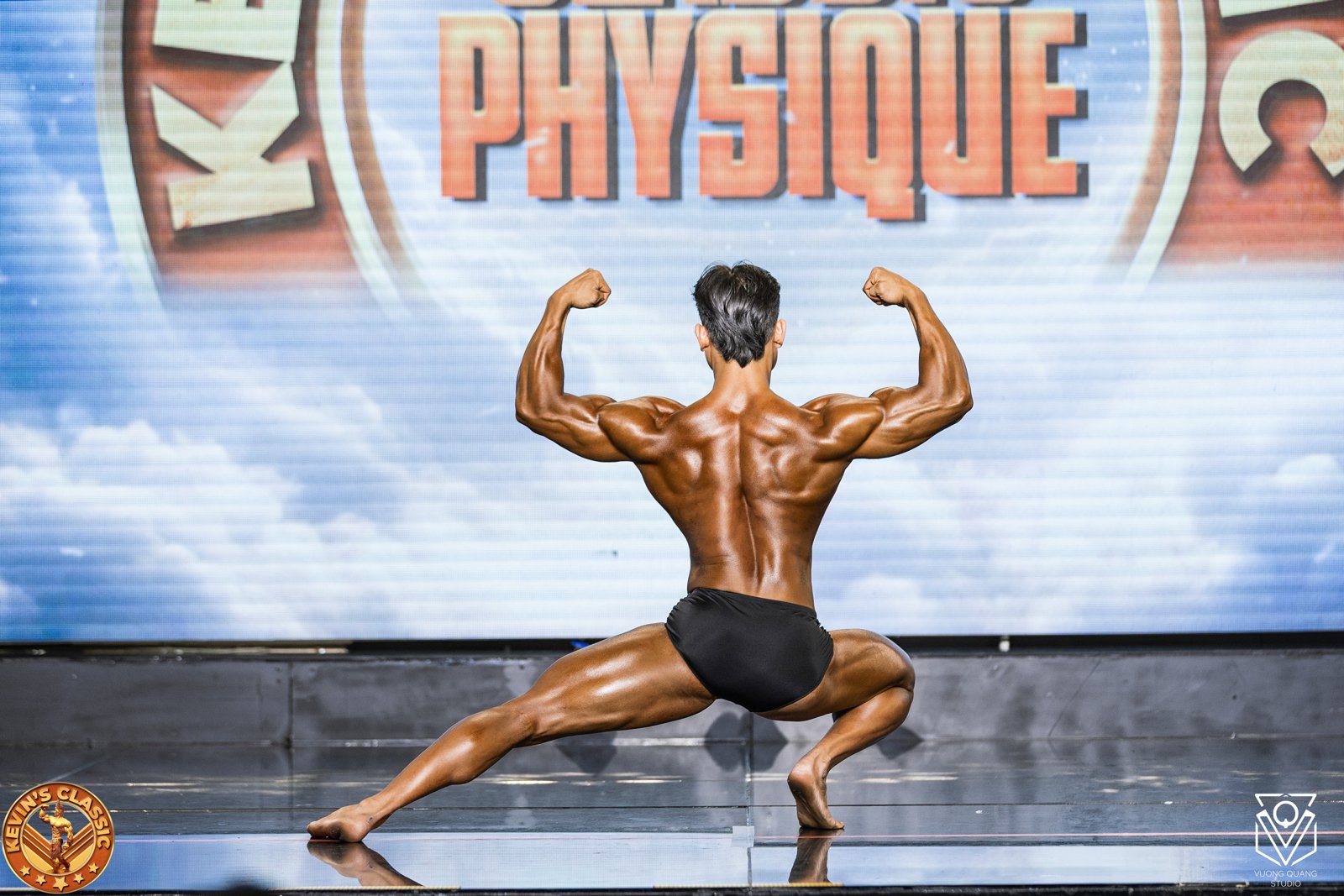 Vận động viên tạo dáng quỳ khoe cơ lưng trước phông Physique