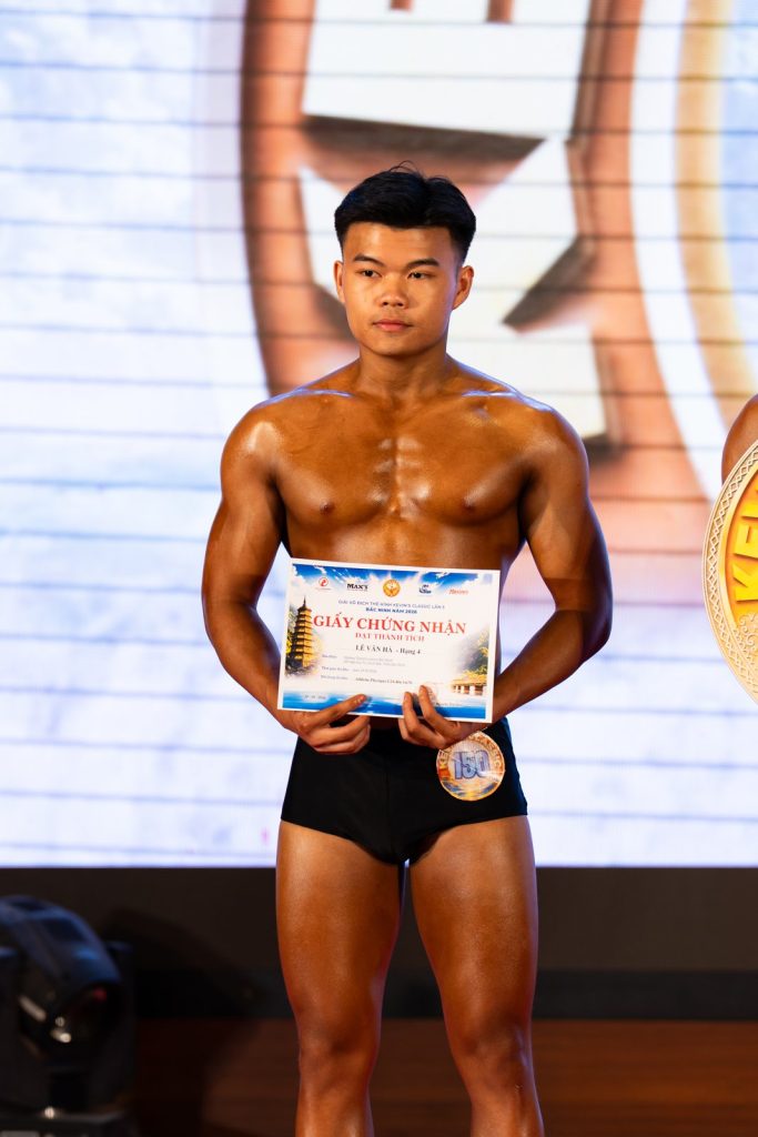 Cận một vận động viên nam trẻ da nâu bóng cầm giấy chứng nhận trước bụng, nền màn LED sáng