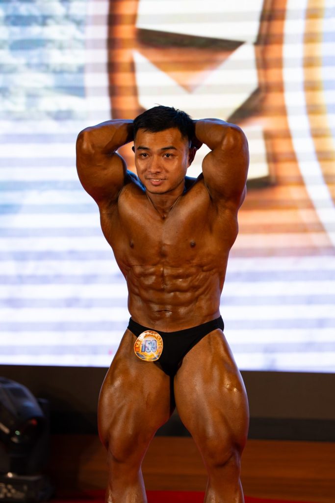 Cận một vận động viên bodybuilding nam tư thế bụng-đùi hai tay sau đầu, da nâu bóng thấy rõ múi cơ