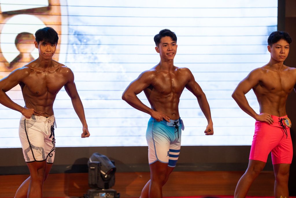 Cận ba vận động viên Men Physique nửa người, màu da nhạt hơn hẳn nhóm thể hình, dễ so sánh độ phủ màu