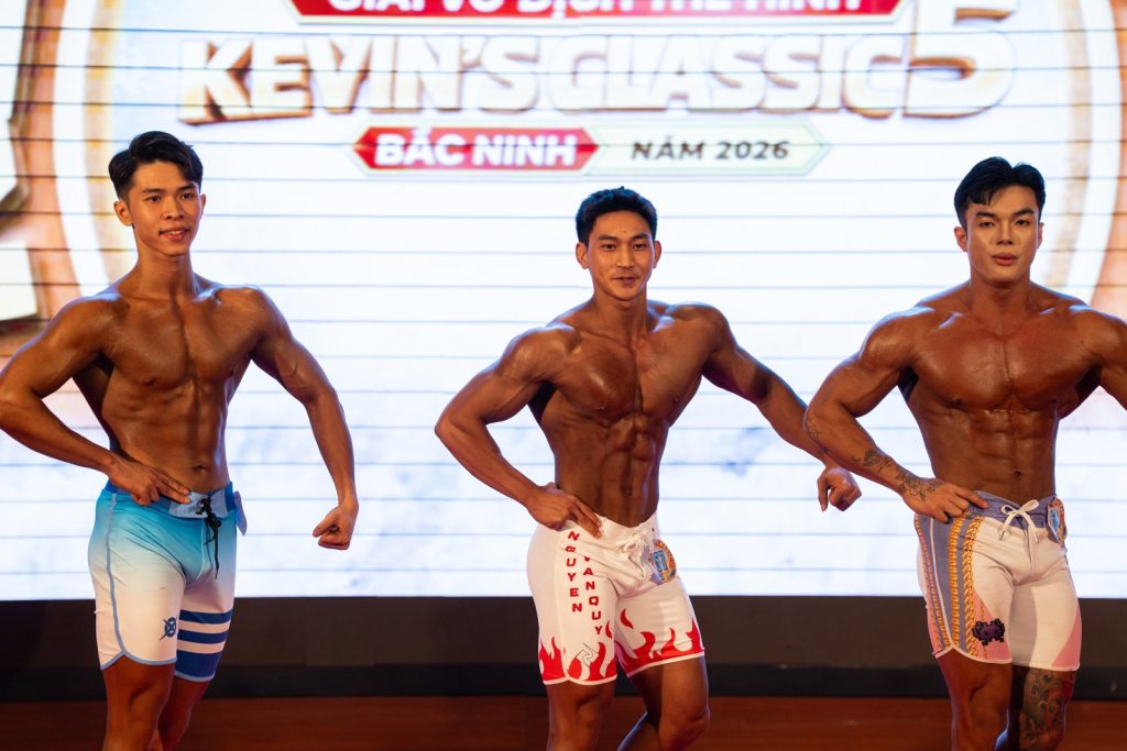 Ba vận động viên Men Physique đứng sát nhau, da nâu bóng, 3 tông đậm nhạt khác nhau, nền Kevin's Classic 5