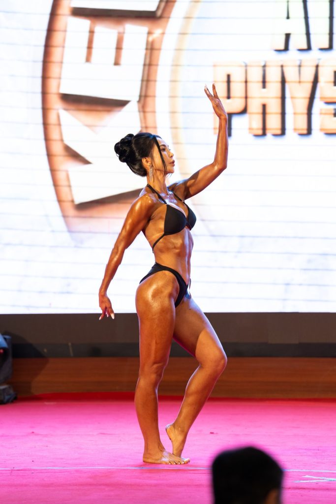 Một vận động viên Athletic Physique nữ đồ đen, nghiêng người, một tay vươn cao trong bài biểu diễn tự do