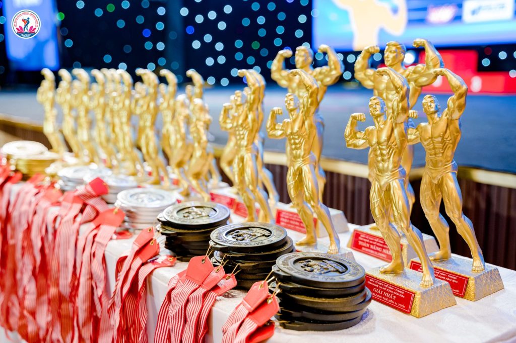 Dãy cúp tượng lực sĩ màu vàng và huy chương của giải thể hình Nghệ An 2026