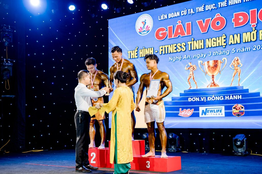Đeo huy chương cho vận động viên trên bục, người áo dài bưng khay tại giải thể hình Nghệ An 2026