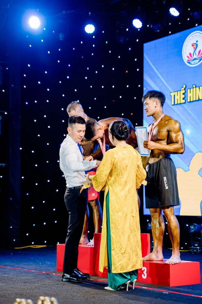 Ông Nguyễn Song Hào, Chủ tịch Liên đoàn Cử tạ, Thể dục, Thể hình tỉnh Nghệ An, đeo huy chương cho vận động viên trên bục – giải thể hình Nghệ An 2026