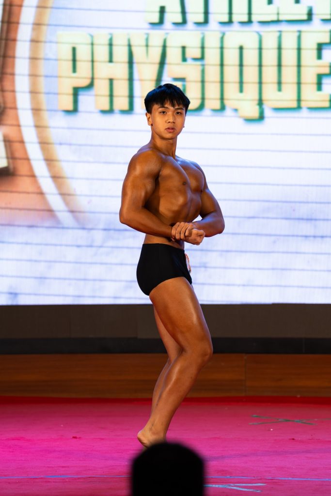 Vận động viên trẻ tạo dáng ngực nghiêng, phía sau là phông chữ Athletic Physique
