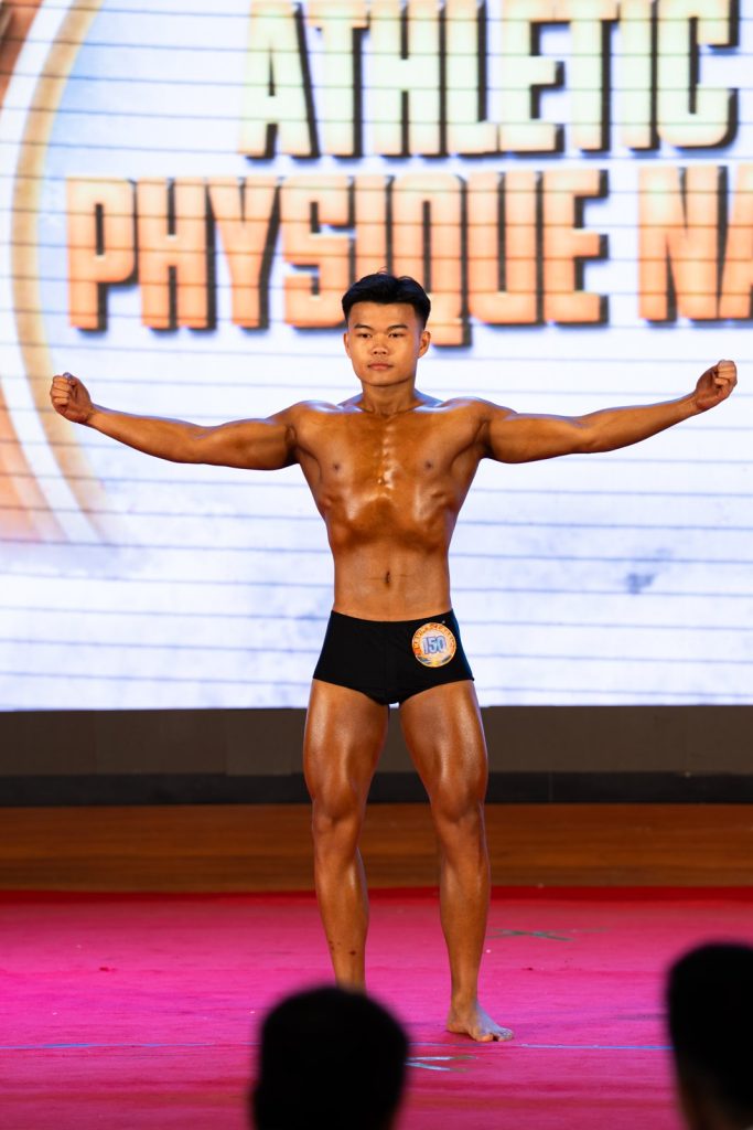 Vận động viên trẻ dang rộng hai tay trong bài tự do, phía sau là phông chữ Athletic Physique Nam