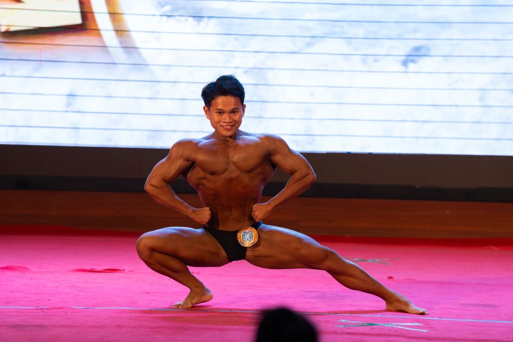 Vận động viên trẻ tấn thấp, hai tay chống hông, cười trong bài tự do
