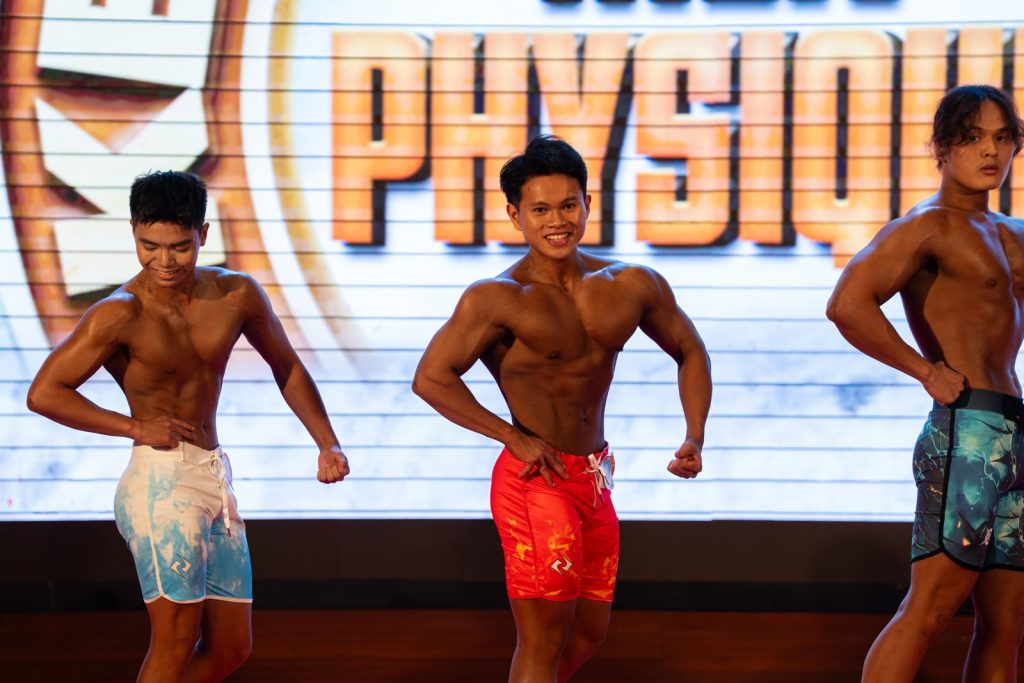 Ba vận động viên trẻ quần short rộng tạo dáng mặt trước, phía sau là chữ Physique