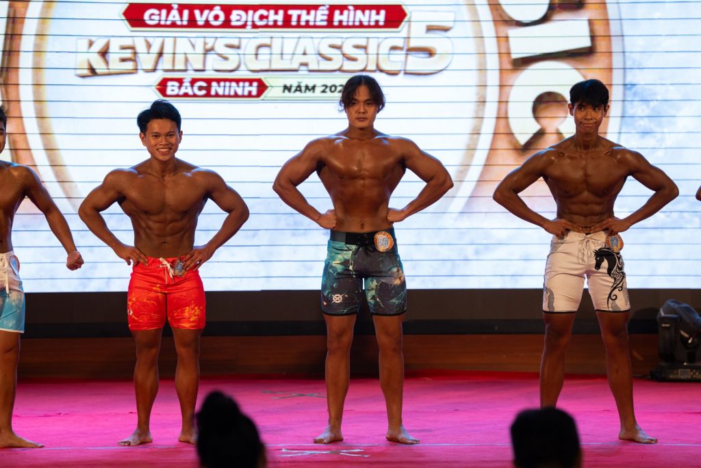 Ba vận động viên trẻ quần short rộng tạo dáng mặt trước, phía sau là logo Kevin’s Classic 5