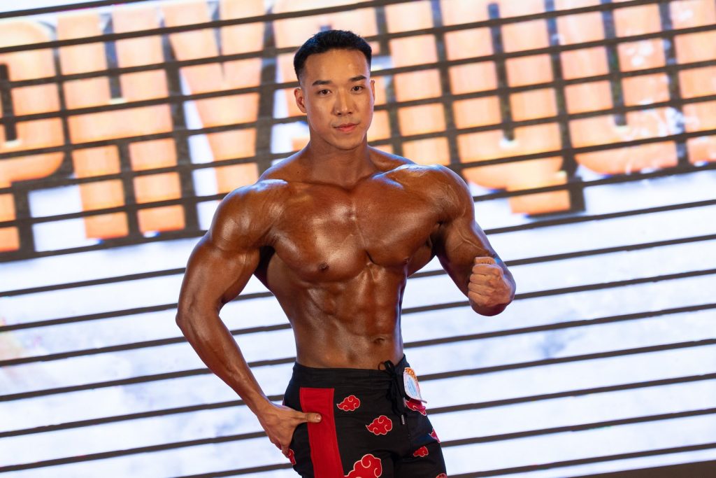 Vận động viên quần short đen họa tiết đỏ tạo dáng mặt trước, trước phông chữ Physique