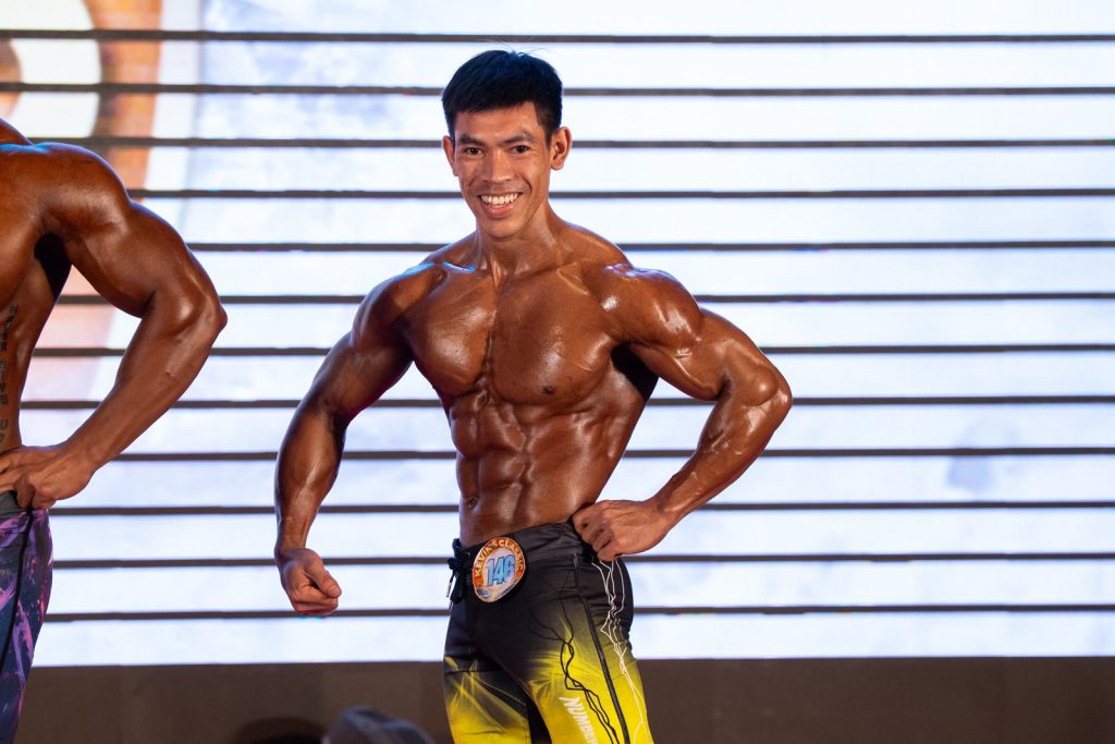 Vận động viên quần short vàng đen tạo dáng mặt trước, hai tay chống hông, cười