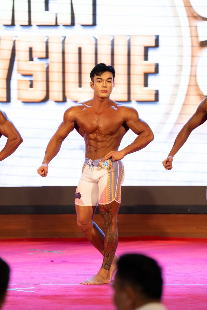 Vận động viên quần short trắng tạo dáng mặt trước, đứng toàn thân trước phông chữ Men Physique