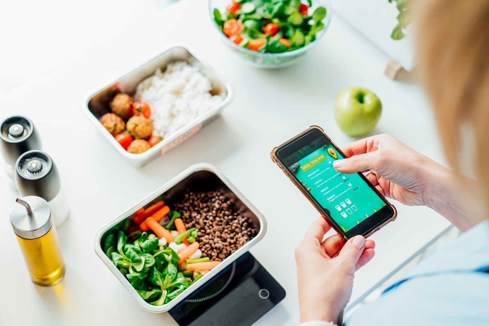 Hộp cơm chia khẩu phần cạnh điện thoại mở ứng dụng ghi lượng ăn