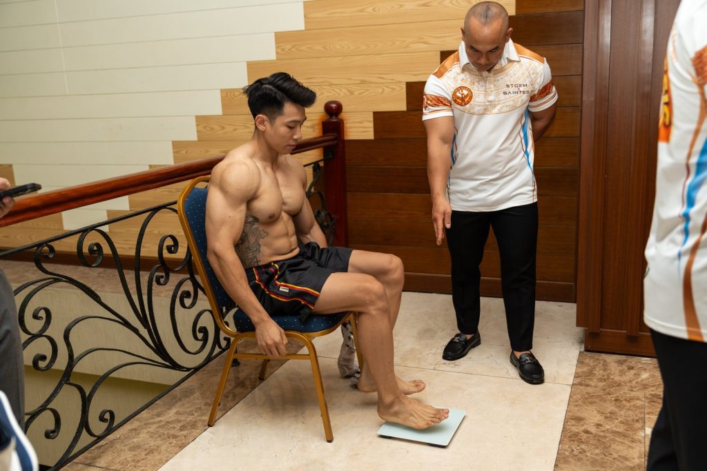 Vận động viên ngồi ở khu cân đo, cạnh thành viên ban tổ chức