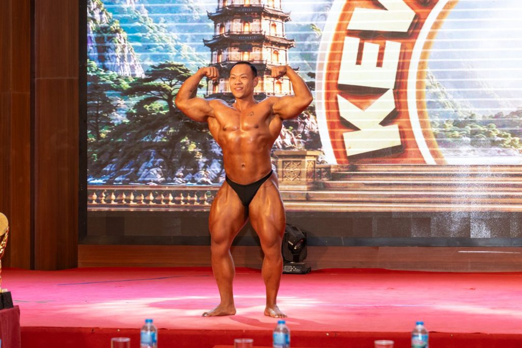 Vận động viên gồng hai tay trước trên sân khấu, phía sau là phông Kevin’s Classic
