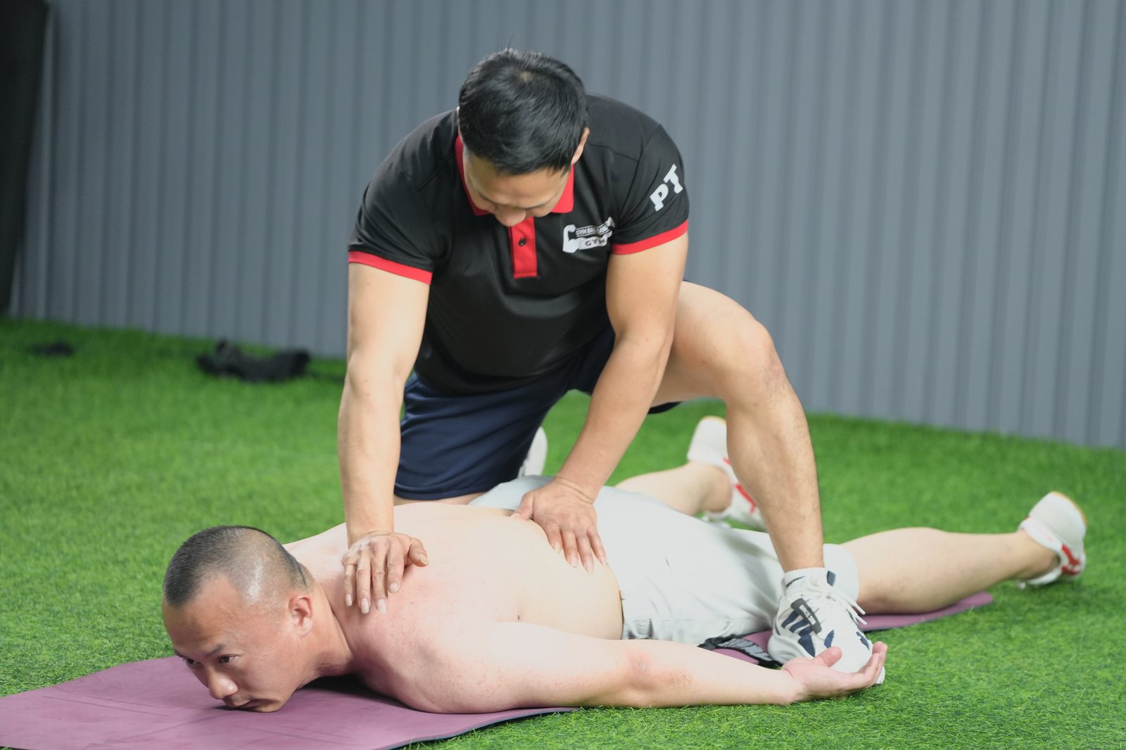 Huấn luyện viên đứng cạnh hỗ trợ học viên trong phòng tập